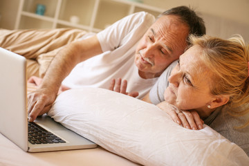 Senior couple in bed using laptop and watching something.