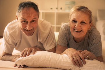 Senior couple lying together in bed and looking at camera.