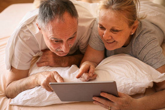 Senior couple enjoying at home and watching something on the tablet before sleeping.