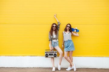 Happy women friends standing over yellow wall