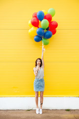 Woman standing over yellow wall. Have fun with balloons.