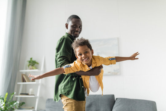 afro father and son playing at home, pretending airplane