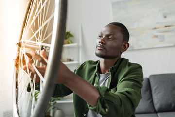 close-up view of pensive afro man checking bicycle wheel at home