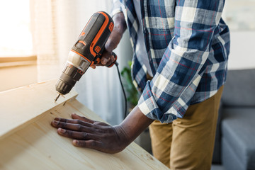 cropped shot of african-american man with perforator applying screw into wood
