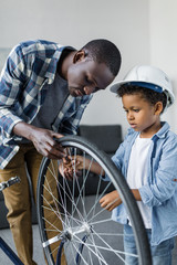 Fototapeta na wymiar african-american father and son in hardhat repairing bicycle