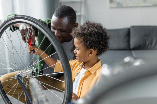 african-american father and son repairing wheel of bicycle