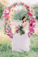 The portrait of the cute bride holding the bouquet of flowers and sitting in the wedding peonies...