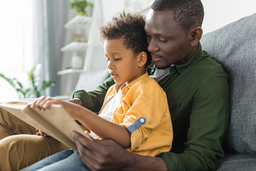 cute african-american father and son reading book together