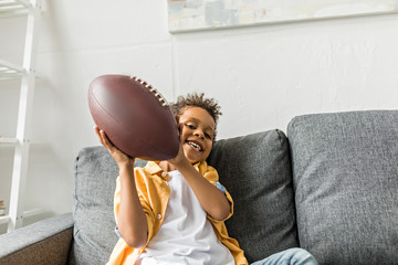 afro boy with american football ball indoor, sitting on sofa