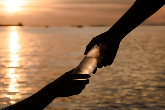 silhouette of Two hands helping/holding Fresh water in bottle,Selective focus and Warm light,hand holding concept