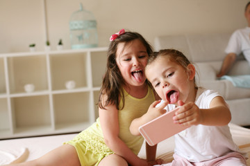 Two little girls at home. Two little girls making self-picture on bed.