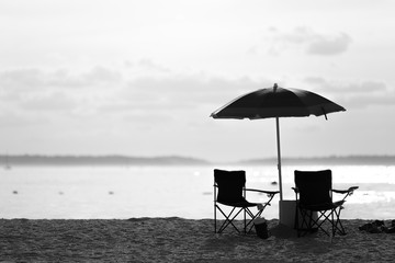 Black and white of lounges chairs and umbrella on the beach in a hot summer day.