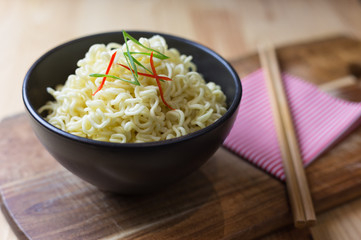 Instant noodles in black bowl on wood background, Asian meal on a table