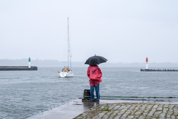 A woman is standing in a harbor in the rain and looks at the water