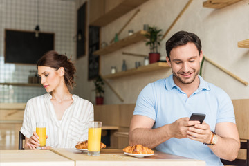 addicted smiling man using his smartphone and unhappy woman sitting on background