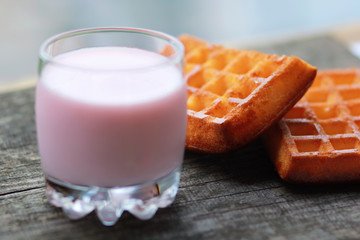 Glass of raspberry yogurt and two freshly baked waffles against blurred blue background on old grey wooden table