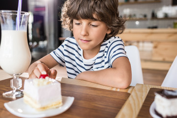 cute little boy with piece of cake in cafe
