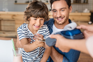 happy son and father paying with credit card in cafe