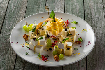 Gourmet cheese set of parmesan, gouda, gorgonzola, brie, camembert and other cheeses on plate. Cheese platter with fruits and appetizers on a wooden table. Close-up.