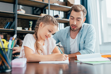 handsome young father doing homework with adorable daughter