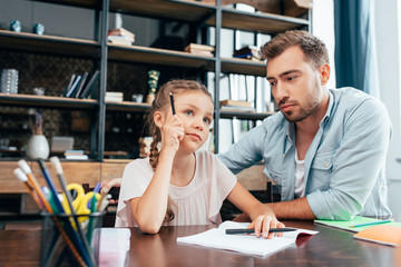 young father doing homework with little thoughtful daughter