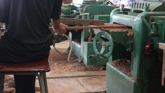 Rear view of worker is working with electric planer of wood machine.