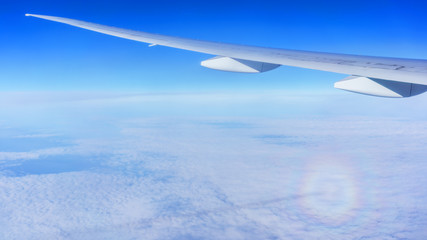 Looking thru airplane 's window seeing an atmospheric optical phenomenon associated with the refraction of sunlight below wing of airplane  , white clouds and blue sky