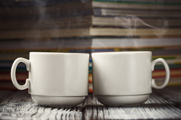 Two hot coffee cups over defocused pile of books