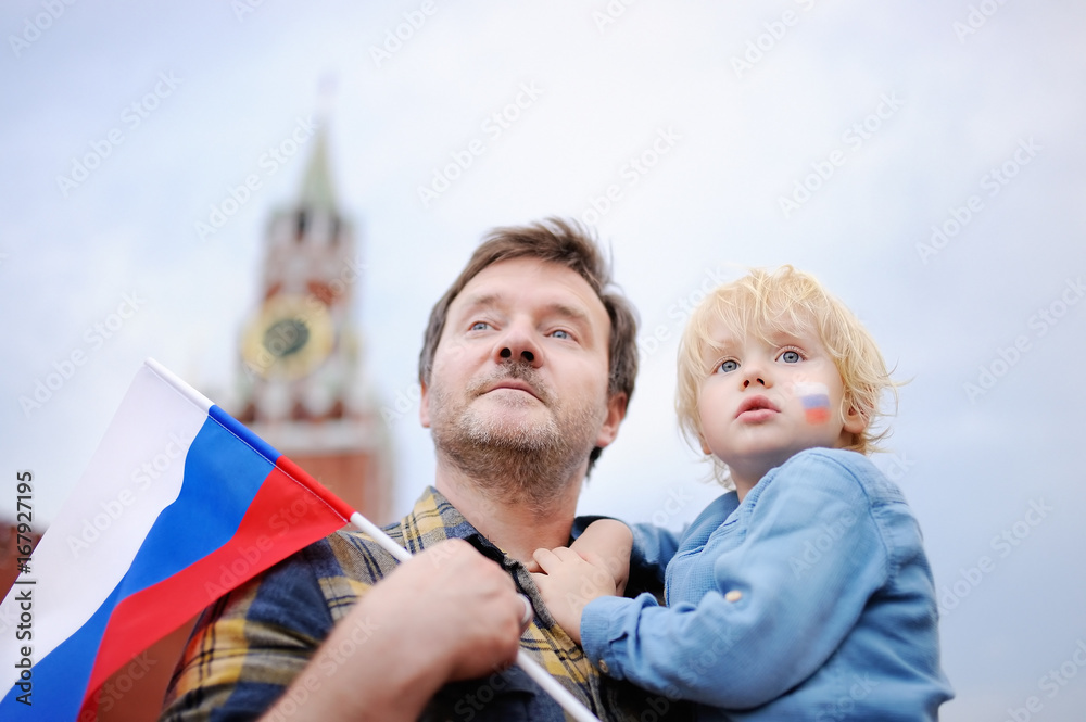 Wall mural Middle age man and his little son with russian flag with Spasskaya tower (Russia, Moscow) on background