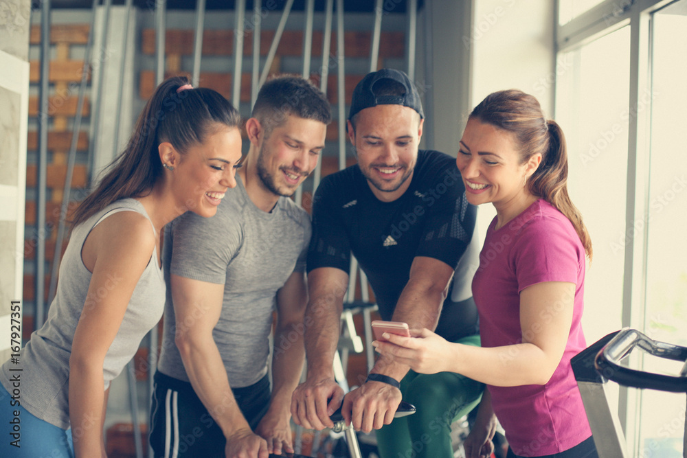 Wall mural Young people in gym. Friends workout in gym and using smart phone. Watching something on phone.