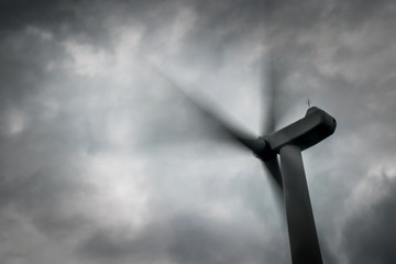Motion blur of electricity windmill turbine sails rotating under grey sky.