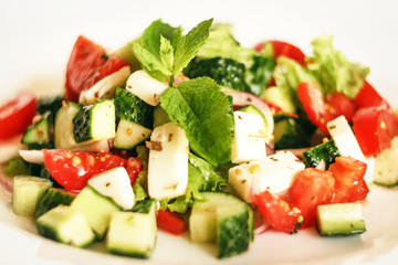 Salad of cucumbers, tomatoes, mozzarella cheese, lettuce, onions, spices and olive oil. Healthy food. Tomato, cucumber, mozzarella cheese, onion, lettuce.