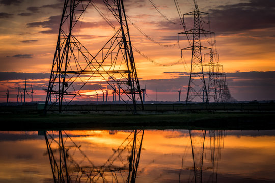 Electricity pylons disappear over horizon on marshland at sunset