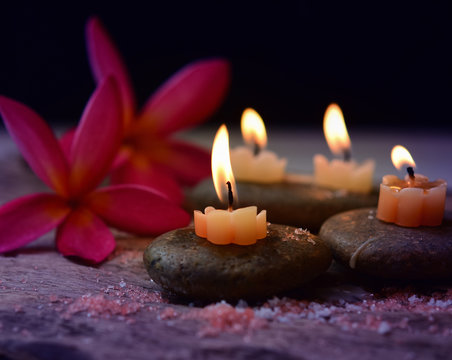 Soft Light and candles scented with refreshing fragrance and salt scrub on black stones, including plumeria flower, spa concept, Thai massage on black background.