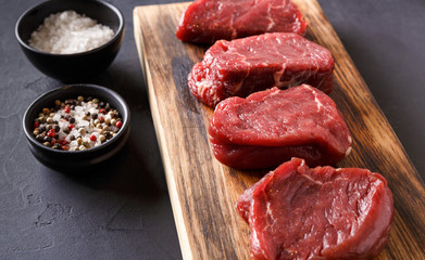 Raw beef filet mignon steaks with spices on wooden board at black background