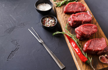 Filet mignon steaks and spices on wood at black background