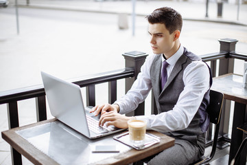 Handsome businessman wearing suit and using modern laptop outdoors, successful manager working in cafe during break and searching information in internet on his notebook computer