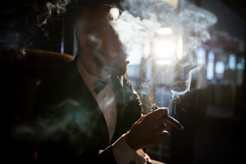 A brutal man in a dress coat smokes a cigar.