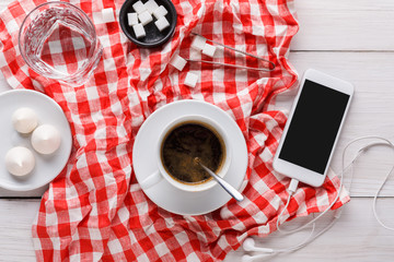 Coffee cup and smartphone on checkered cloth at white wood