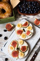 Bagels with fig and banana on curd cheese for breakfast on white rustic cutting board
