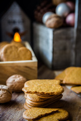 Stack of whole and broken Christmas gingerbread cookies in wood box, lit candle, pine cones and colorful baubles, rustic kitchen interior, festive