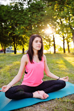 Girl in pink t-shirt practicing yoga sitting on green grass
