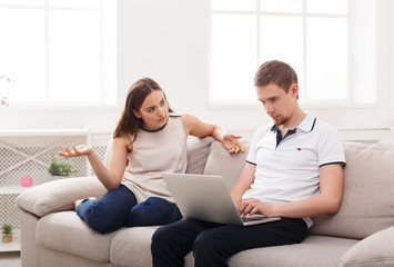 Angry woman sitting while husband using laptop