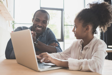 happy african-american father and daughter sitting in cafe with laptop
