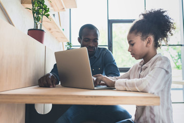 african-american father and daughter sitting in cafe with laptop