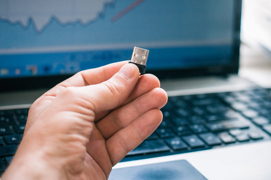 Photographer is holding the Usb adapter with a computer background in the office.