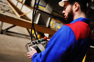 A young handsome worker in a white helmet with a large remote control in the background of the plant.