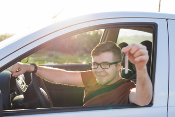 Young man smiling and holding key in his car. Auto purchase and people concept