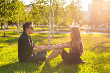 Young happy couple talking together outdoor - sitting on grass