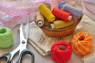 Fototapeta na wymiar Scissors, small basket with spools of threads, piece of cloth and laces with webbing on a linen cloth